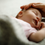 Schlafendes Baby wird liebevoll am Kopf gestreichelt – sichere und geborgene Schlafumgebung - Veronika Hilger