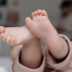 Barfußfüße eines Babys in gemütlicher Kleidung, entspannt auf dem Rücken liegend - Veronika Hilger