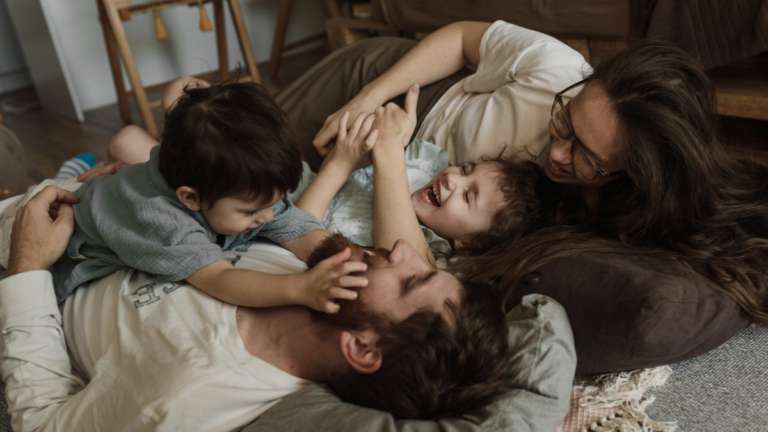 Junge Familie mit zwei Kindern beim Kuscheln – liebevoller Moment des Bindungsaufbaus zwischen Eltern, Baby und Geschwisterkind. Mütterpflege Veronika Hilger