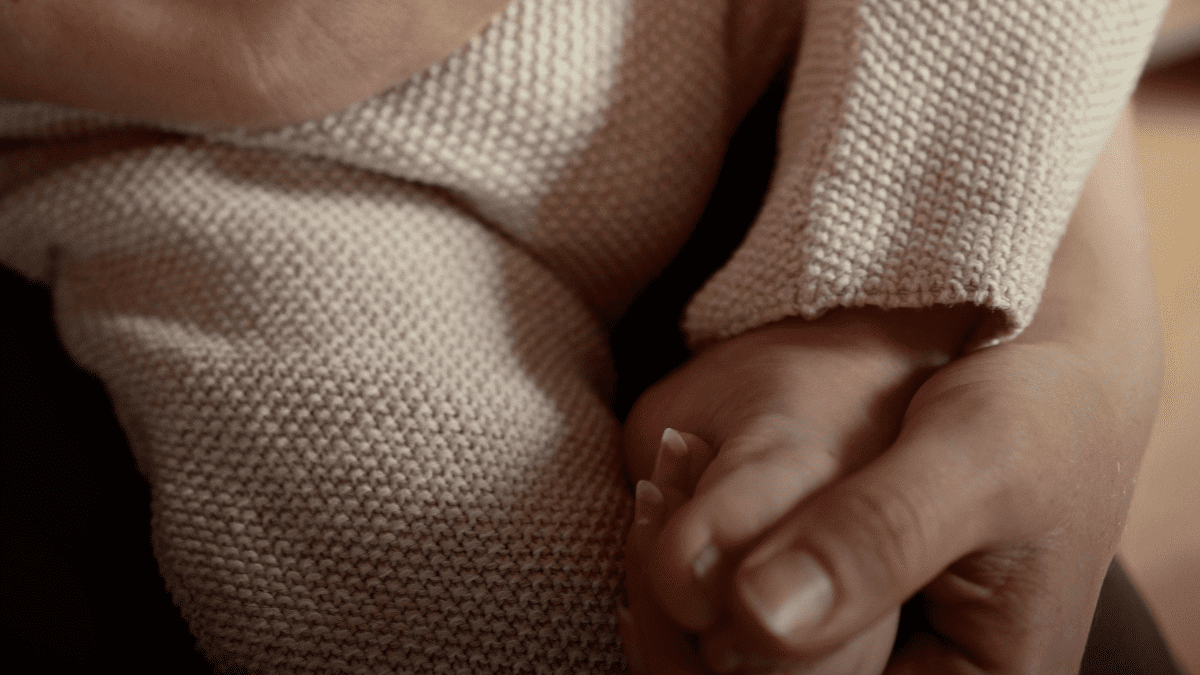 Mutter hält sanft den Fuß ihres Babys – Symbol für Nähe, Vertrauen und Sicherheit beim Wickeln. Baby wickeln ohne Angst.