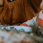 Mutter hält Neugeborenes im Arm vor weihnachtlicher Deko während der Adventszeit. Advent mit Neugeborenem