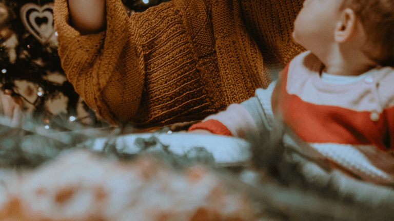 Mutter hält Neugeborenes im Arm vor weihnachtlicher Deko während der Adventszeit. Advent mit Neugeborenem