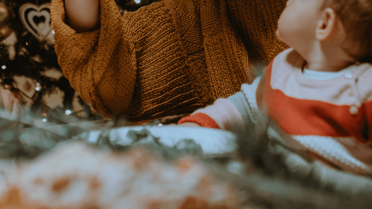 Mutter hält Neugeborenes im Arm vor weihnachtlicher Deko während der Adventszeit. Advent mit Neugeborenem